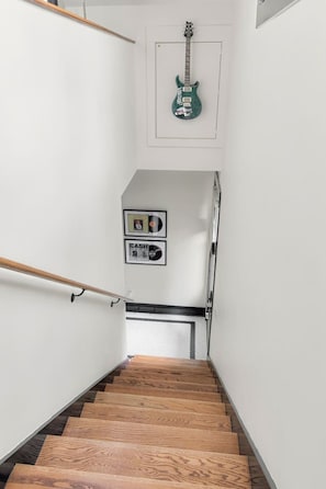 A staircase with wooden steps and metal handrails, leading to a room with a framed picture and a green guitar hanging on the wall.