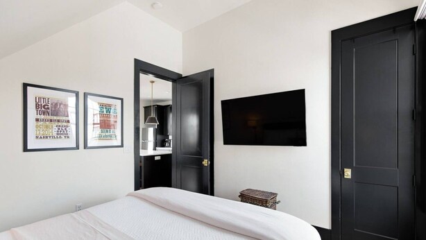 A bedroom with a bed, a television mounted on the wall, and two framed posters on the wall.