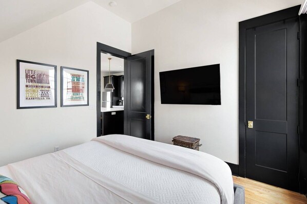 Un dormitorio con una cama, un televisor montado en la pared y dos carteles enmarcados.
