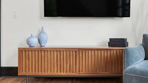 A modern living room with a wooden console table, two vases, a stack of black boxes, and a grey armchair.