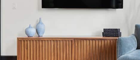 Una sala de estar moderna con una consola de madera, dos jarrones, una pila de cajas negras y un sillón gris.