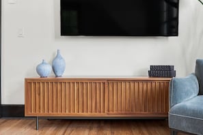 Una sala de estar moderna con una consola de madera, dos jarrones, una pila de cajas negras y un sillón gris.