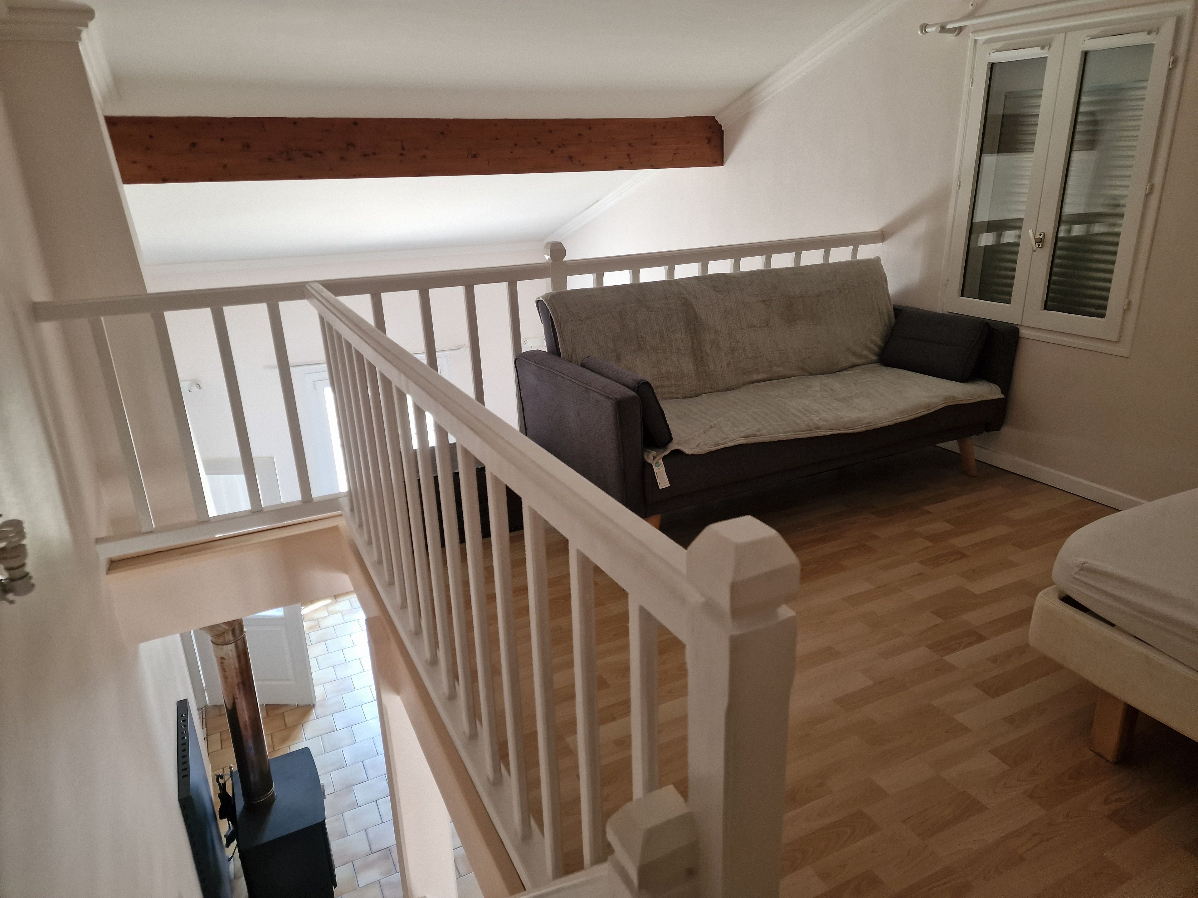 Una habitación con suelo de madera, barandilla blanca, sofá gris y armario blanco.