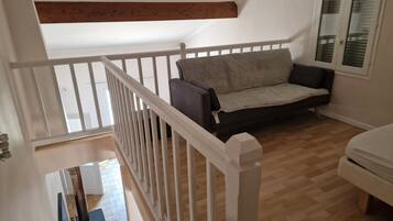 Una habitación con suelo de madera, barandilla blanca, sofá gris y armario blanco.