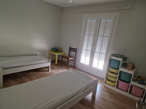 A room with two beds, a small table, a chair, a window with blinds, and storage units with colorful bins.