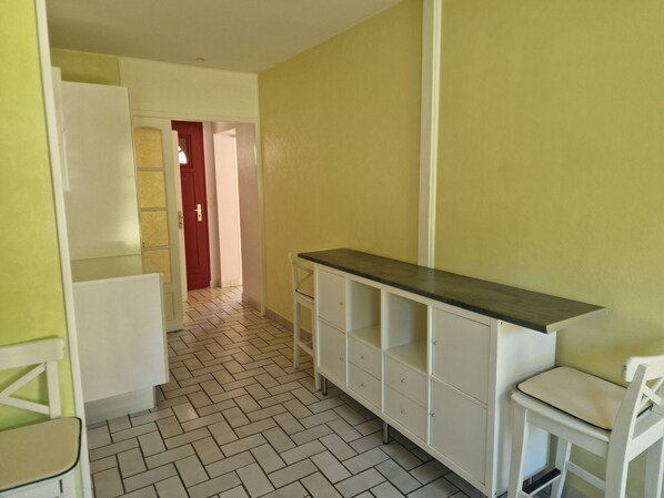 A narrow hallway with a white cabinet, a red door, and a white chair.