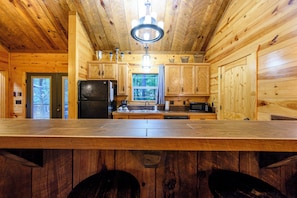 A wooden cabin interior with a kitchen area featuring a refrigerator, microwave, and sink. - Private & Rustic | 2 Kings + Hot Tub + Firepit (Broken Bow)