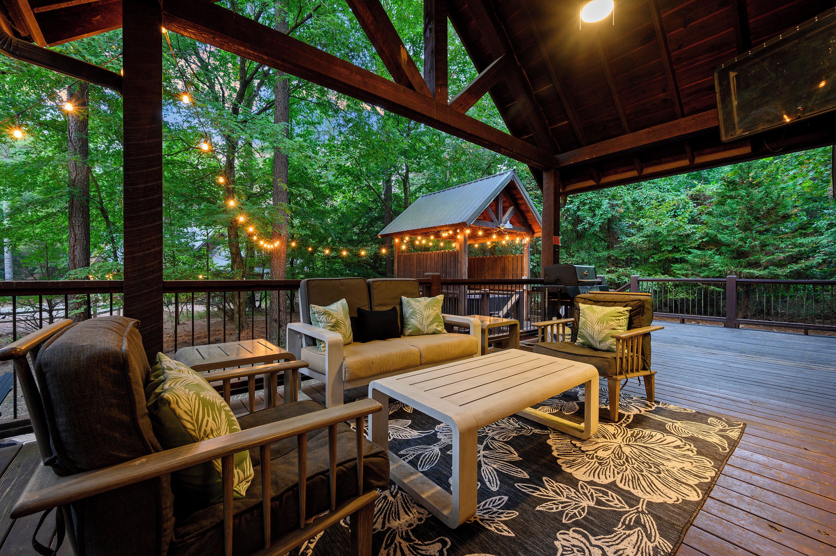 Une terrasse extérieure avec des meubles en bois, des guirlandes lumineuses et un espace abrité doté d’un toit en métal.