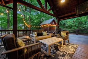 Une terrasse extérieure avec des meubles en bois, des guirlandes lumineuses et un espace abrité doté d’un toit en métal.