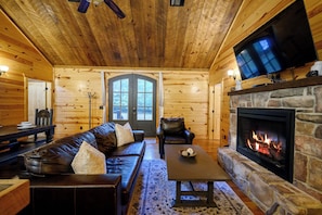 A log cabin interior with a stone fireplace, leather sofa, and a television mounted above it. - Private & Rustic | 2 Kings + Hot Tub + Firepit (Broken Bow)
