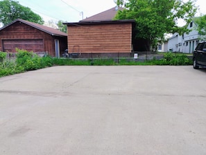 A large, empty concrete parking area with a wooden building and a garage in the background.