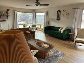 A spacious living room with a green sofa, a brown armchair, a wicker coffee table, and a ceiling fan.
