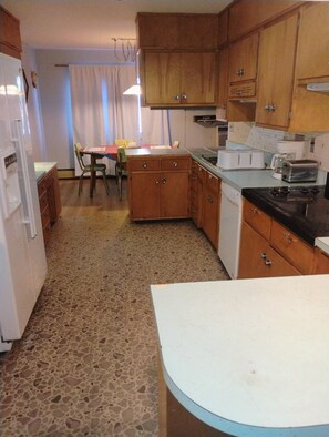 A kitchen with wooden cabinets, a dining table, chairs, a refrigerator, and a stove.