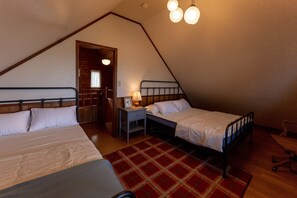 A triangular attic bedroom with two beds, a nightstand, a lamp, and a red plaid rug.