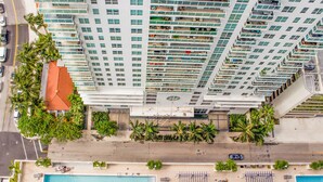 Um edifício alto com várias varandas, piscina e palmeiras.