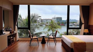 Habitación de hotel con un ventanal grande, una cama, un escritorio, una silla y una pequeña mesa.