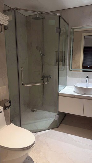 Un baño moderno con ducha envuelta en vidrio, inodoro blanco y lavabo con espejo arriba.