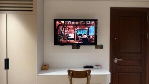 Televisor fixat a la paret sobre un escriptori blanc amb una cadira de fusta al davant.