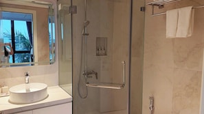 Un baño moderno con cabina de ducha de vidrio, lavamanos redondo y toallero.