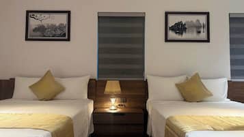 Quarto de hotel com duas camas, mesa de cabeceira com abajur e quadros nas paredes.