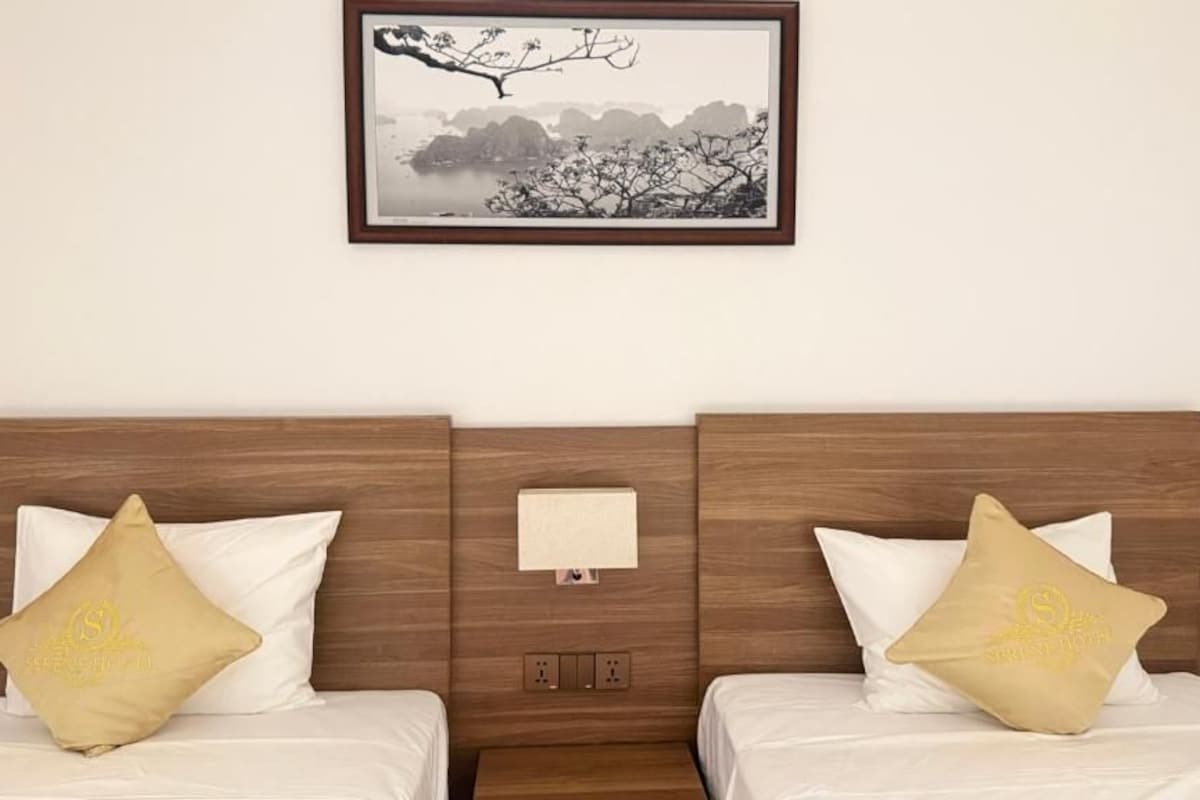 Habitación de hotel con dos camas, una mesita de noche, una lámpara de pared y un cuadro enmarcado sobre las camas.