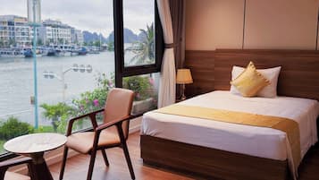 A hotel room with a bed, a chair, a small table, and a view of a river with boats.