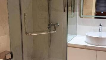 A bathroom with a glass-enclosed shower, a toilet, and a sink with a mirror above it.