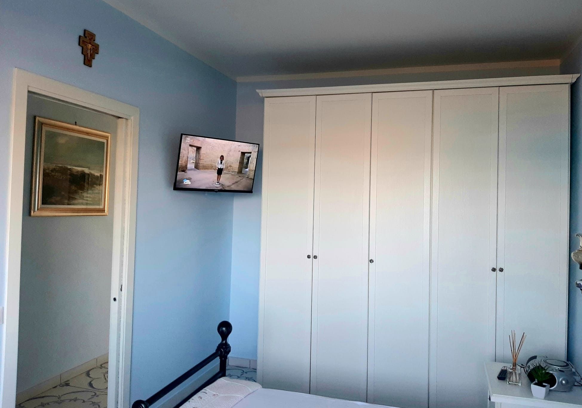 A bedroom with a bed, a wardrobe, a painting, and a television.
