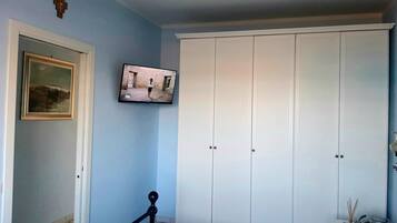 A bedroom with a bed, a wardrobe, a painting, and a television.