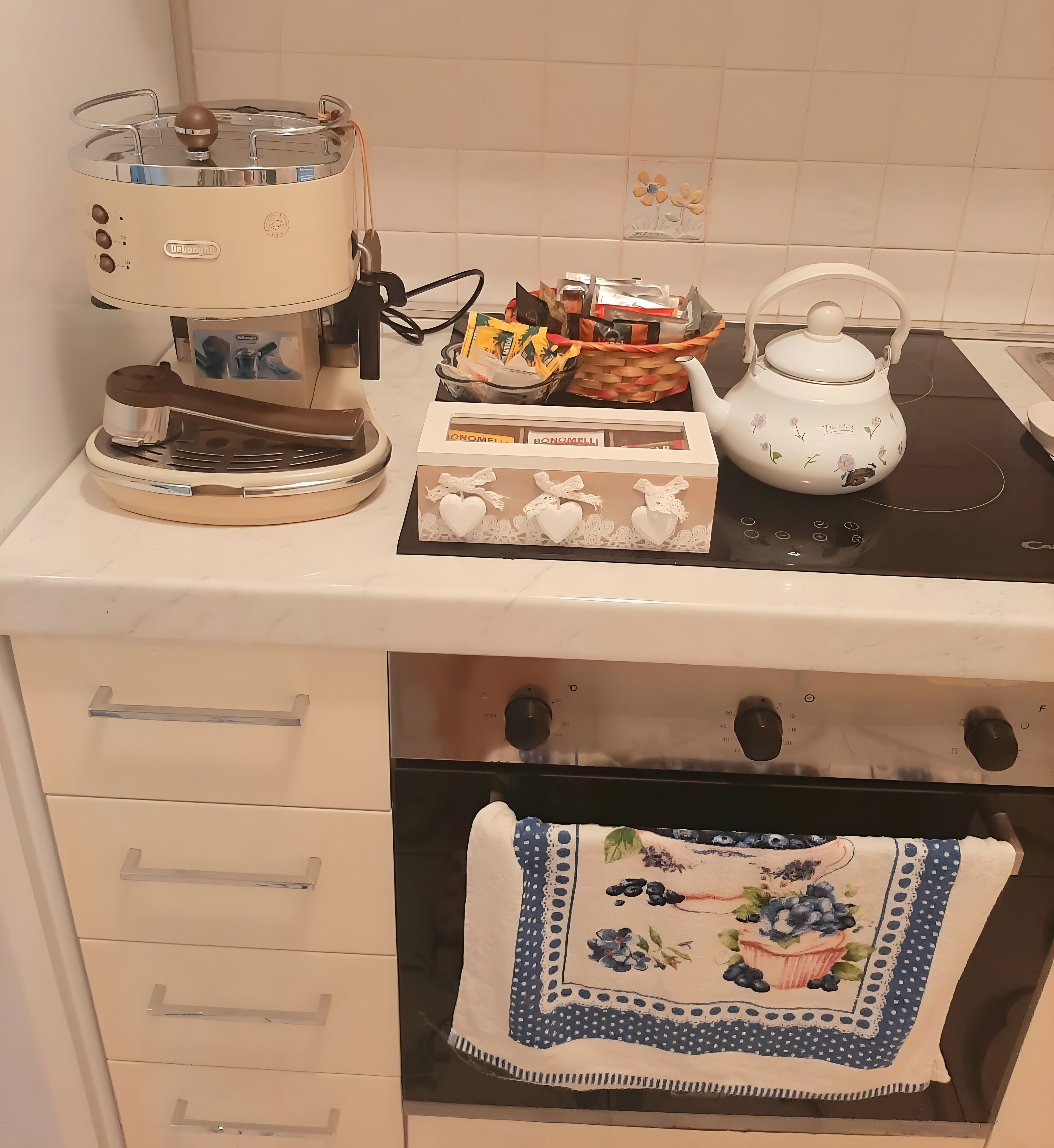 A kitchen with a coffee maker, a basket of snacks, a teapot, and a box of Bonomelli wine.