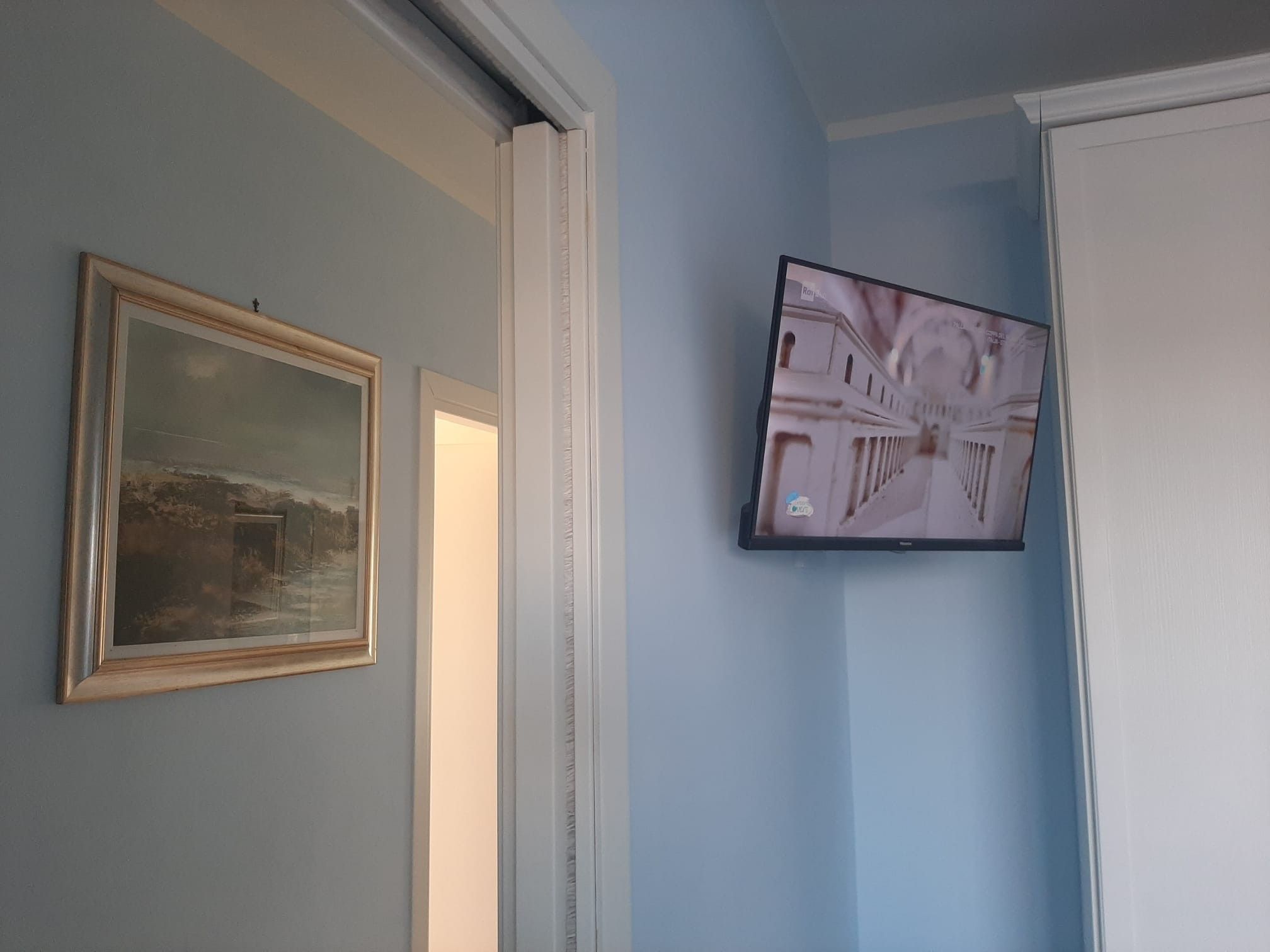 Une pièce avec un tableau encadré accroché au mur, un téléviseur fixé au mur et une porte donnant sur une autre pièce.