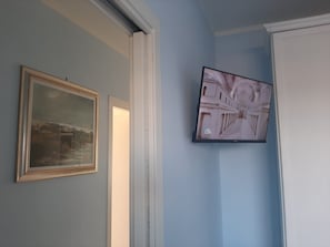 A room with a framed painting on the wall, a television mounted on the wall, and a door leading to another room.