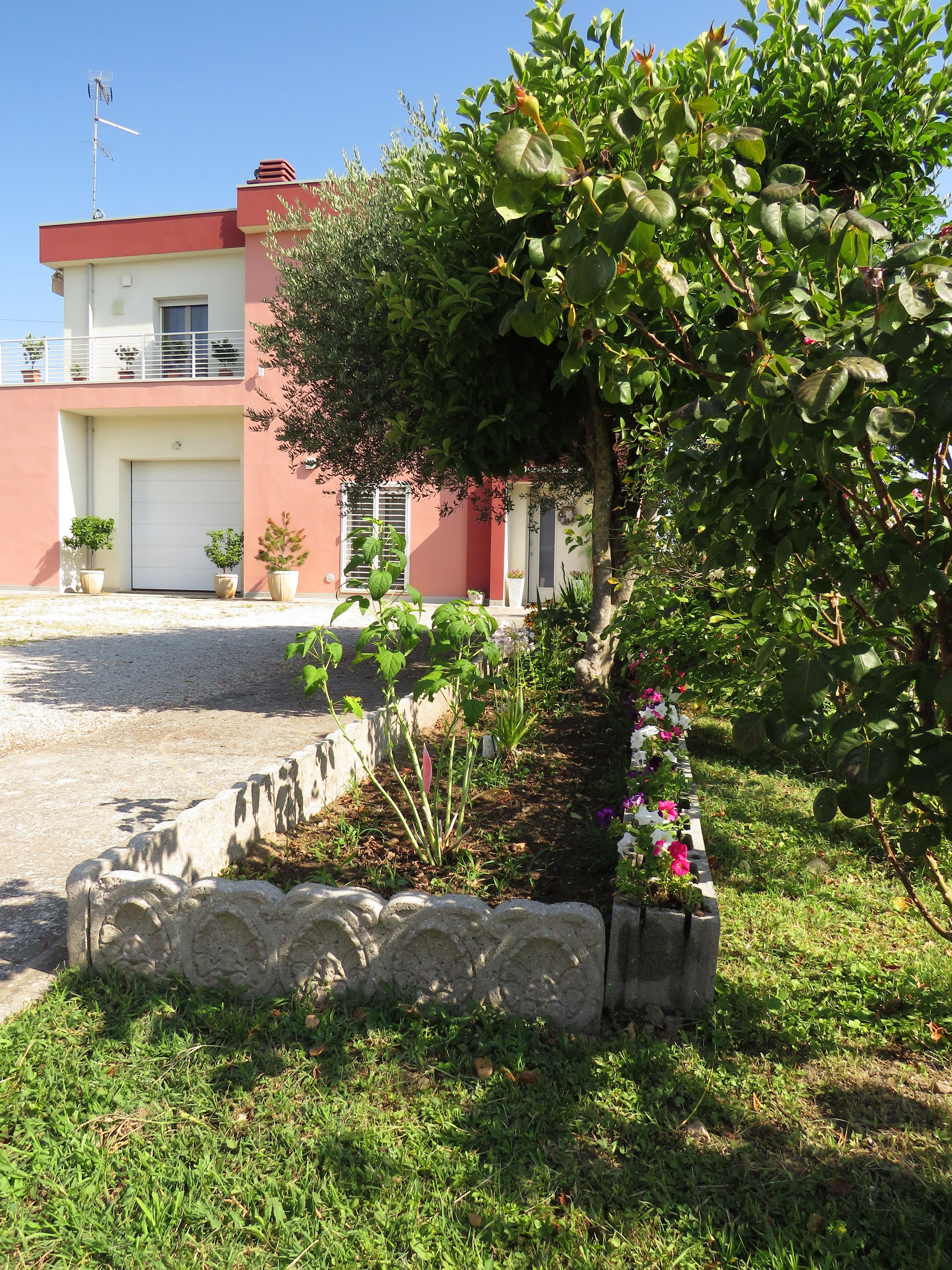 Un bâtiment à la façade rouge, avec une porte de garage et un jardin où poussent différentes plantes et fleurs.