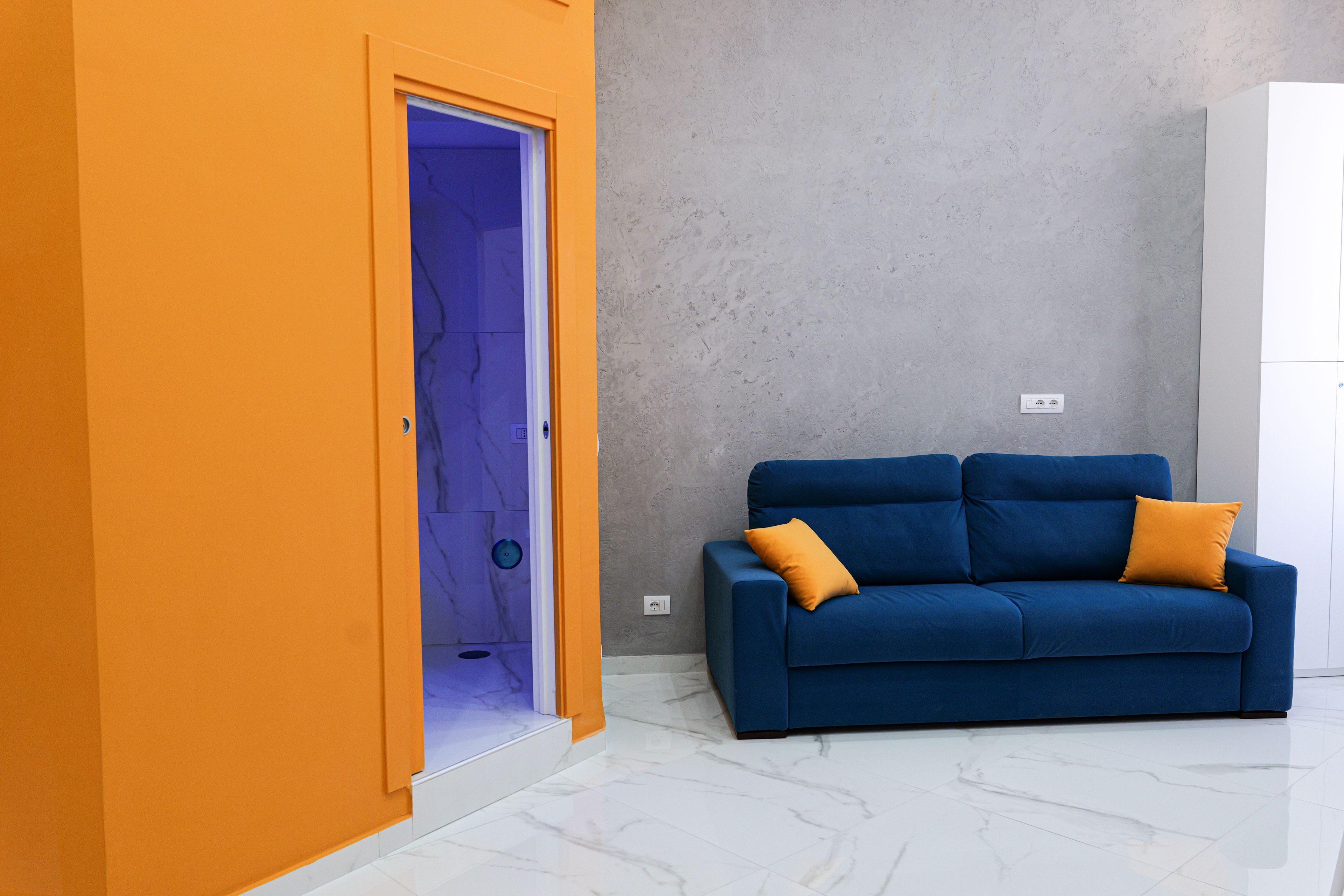 A room with a blue sofa, an orange door, and a grey textured wall.