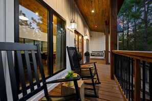 A wooden deck with outdoor seating, large windows, and a view of trees. - Modern Hochatown Cabin - Hot Tub, 2 Kings, Arcade + Firepit (Broken Bow)
