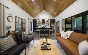 A spacious living area with a wooden ceiling, a dining table, and a sofa. - Modern Hochatown Cabin - Hot Tub, 2 Kings, Arcade + Firepit (Broken Bow)