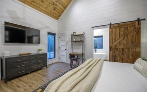 A bedroom with a bed, a dresser, a TV, a wooden door, and a window. - Modern Hochatown Cabin - Hot Tub, 2 Kings, Arcade + Firepit (Broken Bow)