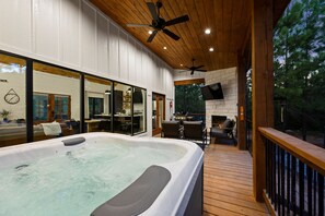 A hot tub on a wooden deck with a stone fireplace and outdoor seating. - Modern Hochatown Cabin - Hot Tub, 2 Kings, Arcade + Firepit (Broken Bow)