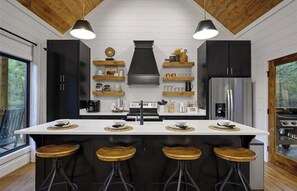 A modern kitchen with a central island, bar stools, and built-in appliances. - Modern Hochatown Cabin - Hot Tub, 2 Kings, Arcade + Firepit (Broken Bow)