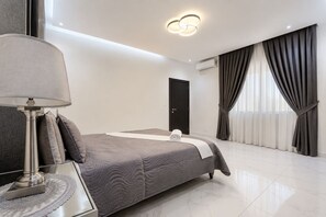 A modern bedroom with a bed, a bedside table with a lamp, a door, and a window with curtains. - Spacious 3-bedroom apartment Dakar Fast Wifi with AC and gym, Centrally Located (Dakar)