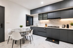 Een moderne keuken met donkere kasten, een marmeren aanrechtblad en een eethoek met witte stoelen.