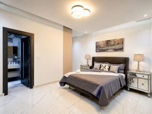 Een moderne slaapkamer met een groot bed, twee nachtkastjes, een wandlamp en een deur naar een badkamer.