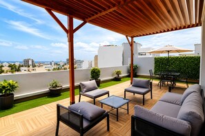 Una terraza en la azotea con mobiliario exterior, vistas de la ciudad y un césped.