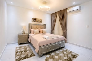 A bedroom with a bed, nightstand, lamp, air conditioning unit, and curtains. - Spacious 3-bedroom apartment Dakar Fast Wifi with AC and gym, Centrally Located (Dakar)