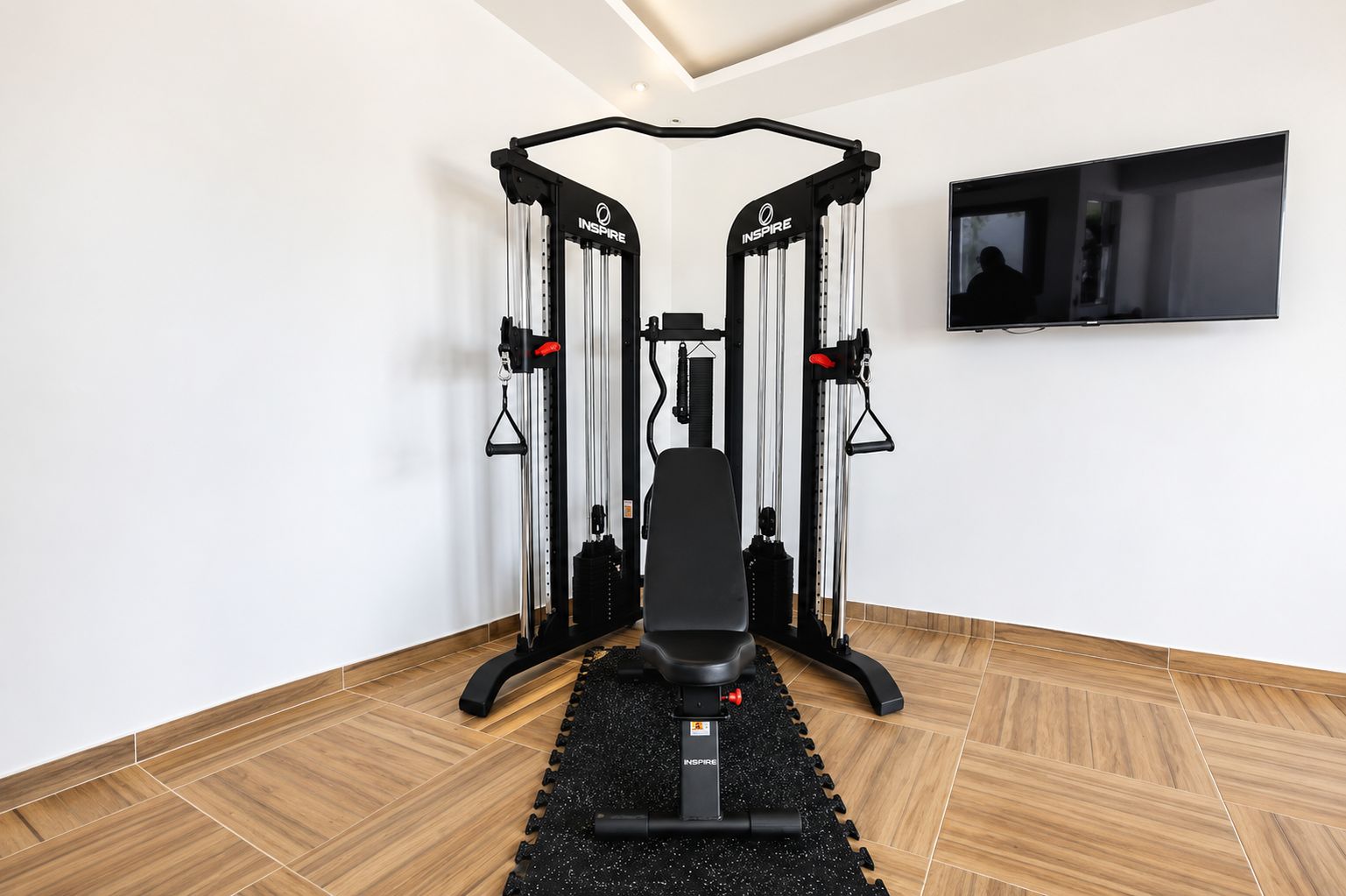 Un gimnasio con bancos, máquinas de pesas y un televisor montado en la pared.