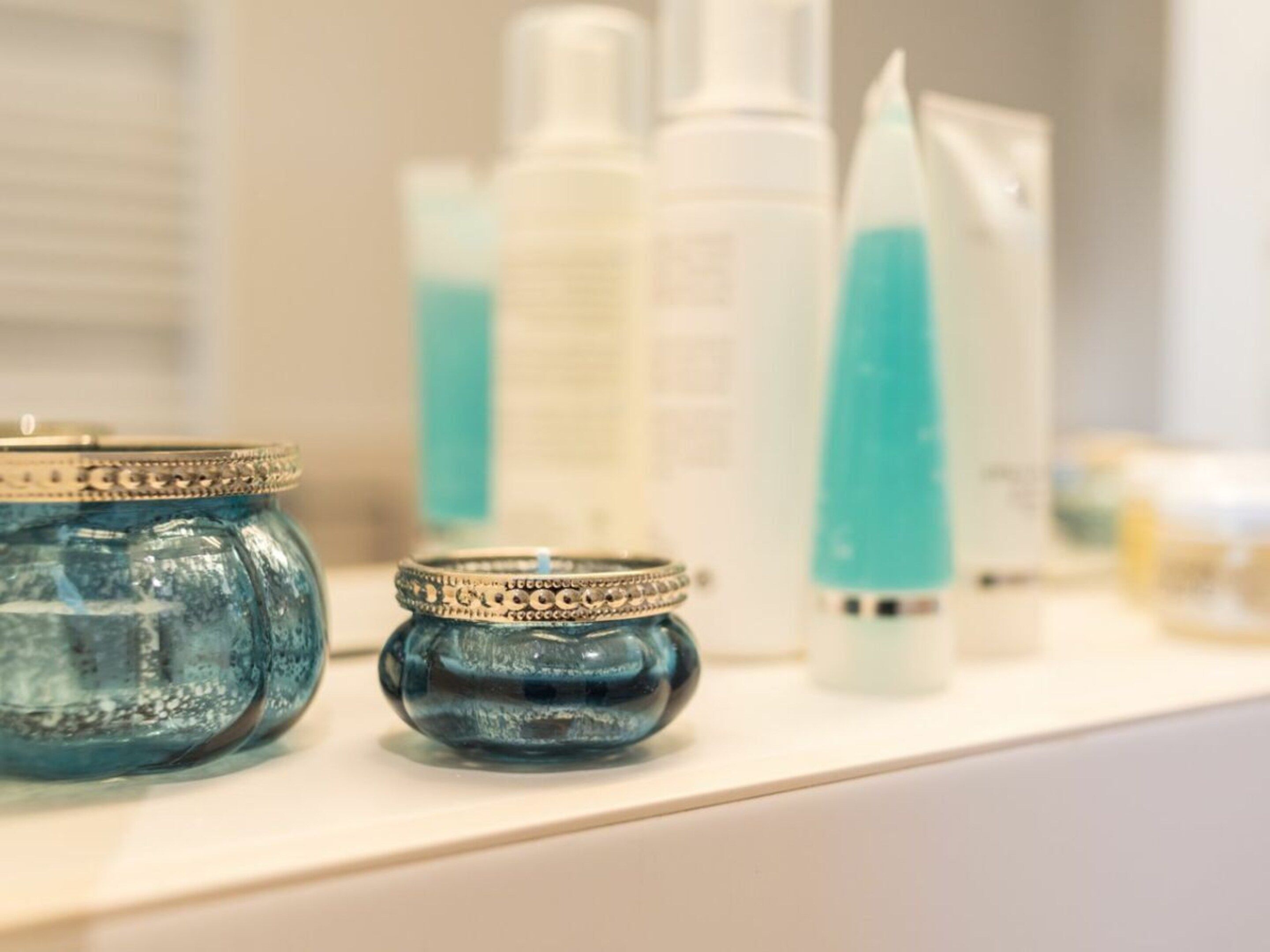 Una encimera de baño con diversos artículos de aseo, incluyendo un frasco de vidrio azul, una botella blanca y un tubo azul.