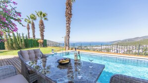 An outdoor pool area with a table set for dining, surrounded by wicker furniture, palm trees, and a view of the sea. - mira villa 2 (Torba)