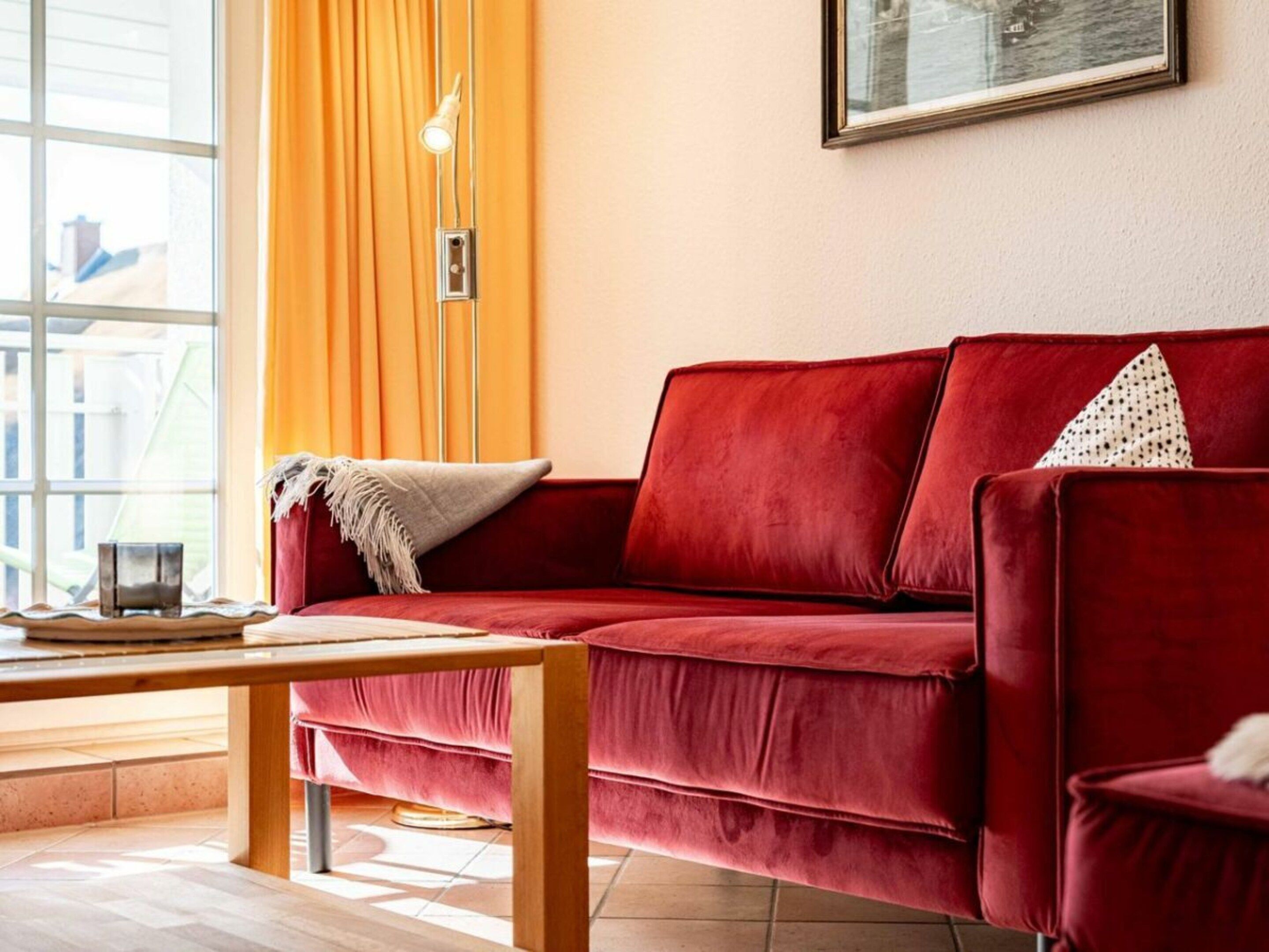 Un sofá rojo con un cojín, una mesa de centro de madera y un cuadro en la pared.