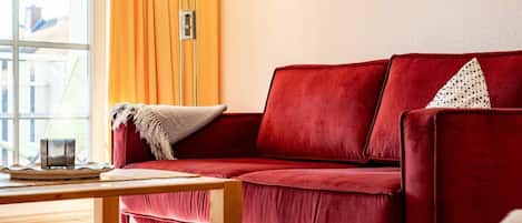 Un sofá rojo con un cojín, una mesa de centro de madera y un cuadro en la pared.