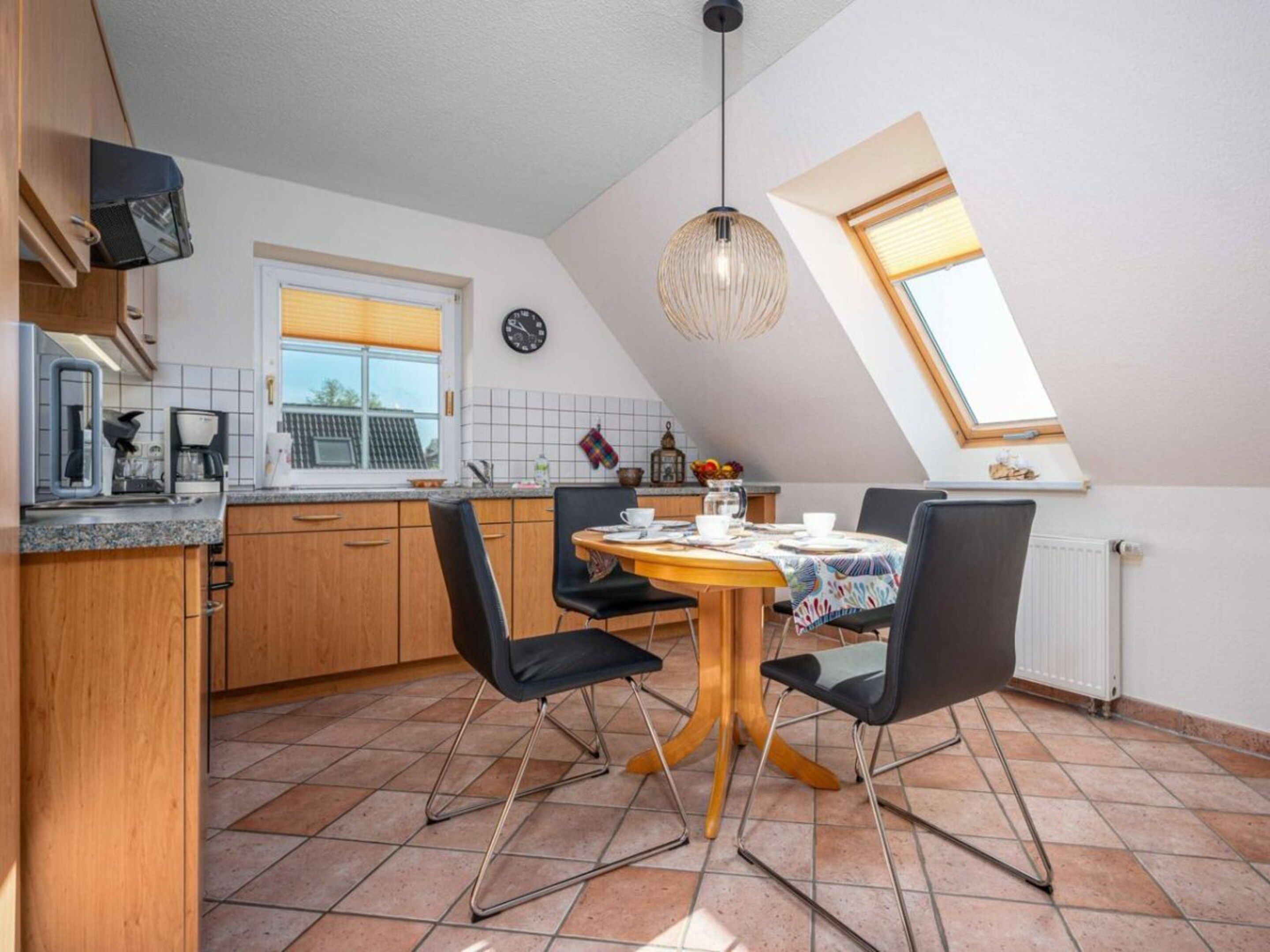 Et køkken med spiseplads, et ur på væggen og et vindue med persienner.